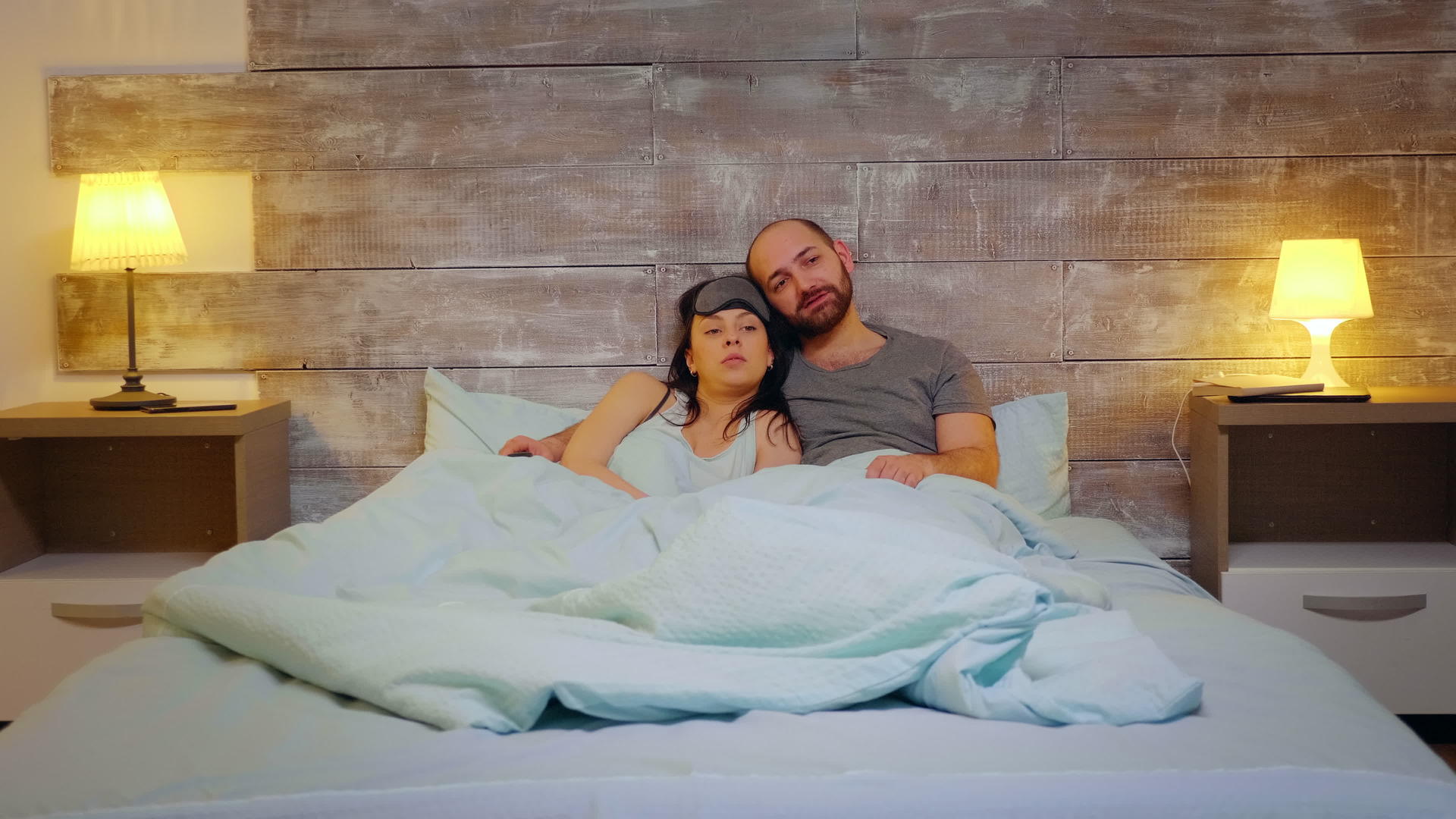 一对幸福的已婚夫妇穿着睡衣躺在床上看电视视频的预览图