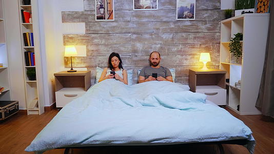 一对夫妇躺在舒适的床上用智能手机监控录音放大镜头视频的预览图