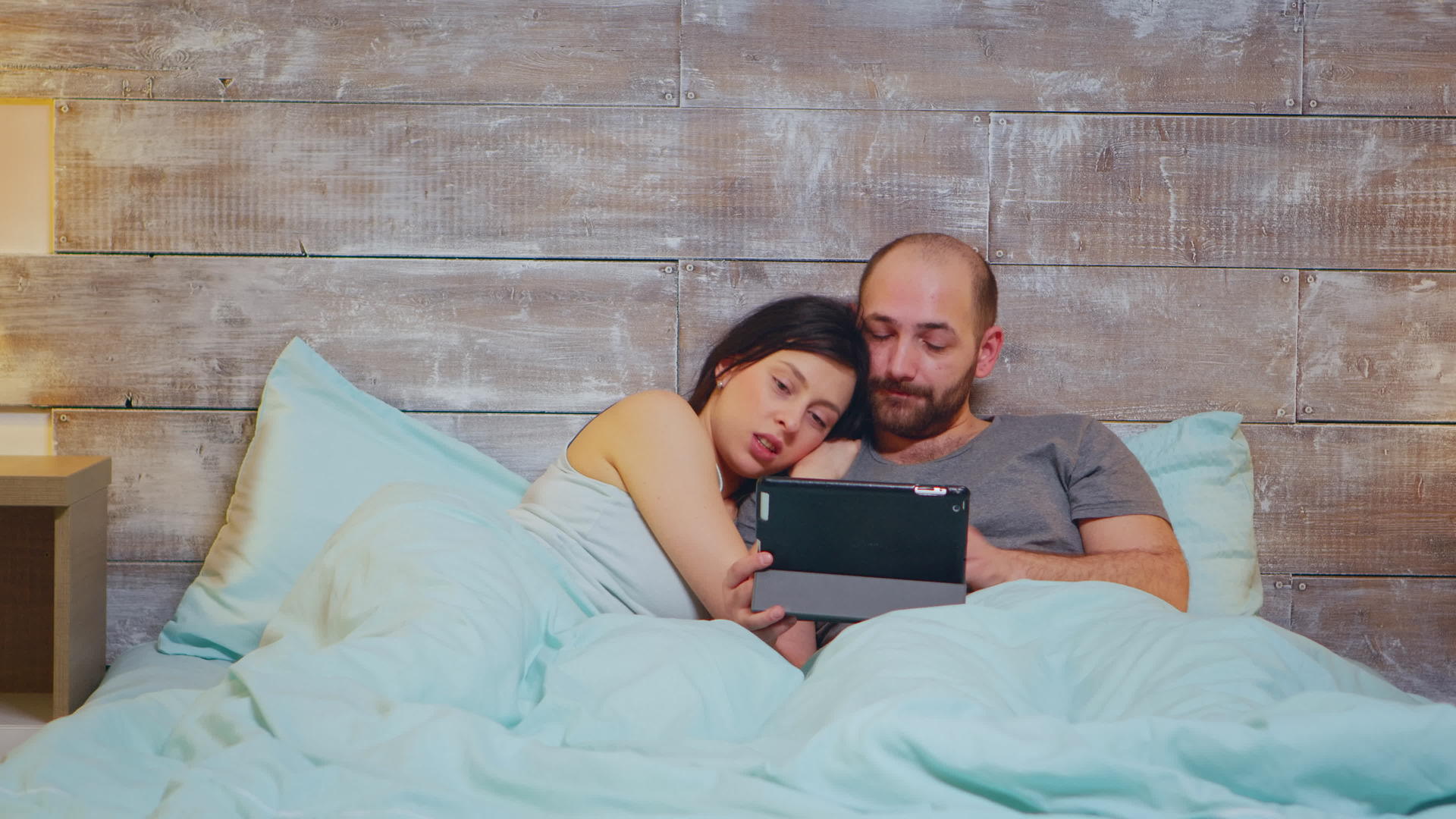 一对夫妇穿着平板电脑的睡衣躺在床上视频的预览图
