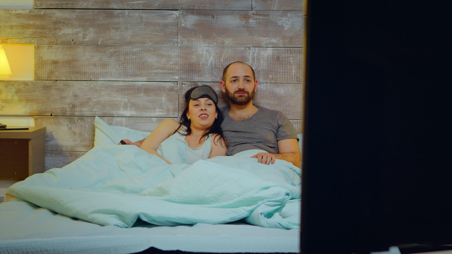 一对夫妇穿着睡衣躺在床上看电视视频的预览图