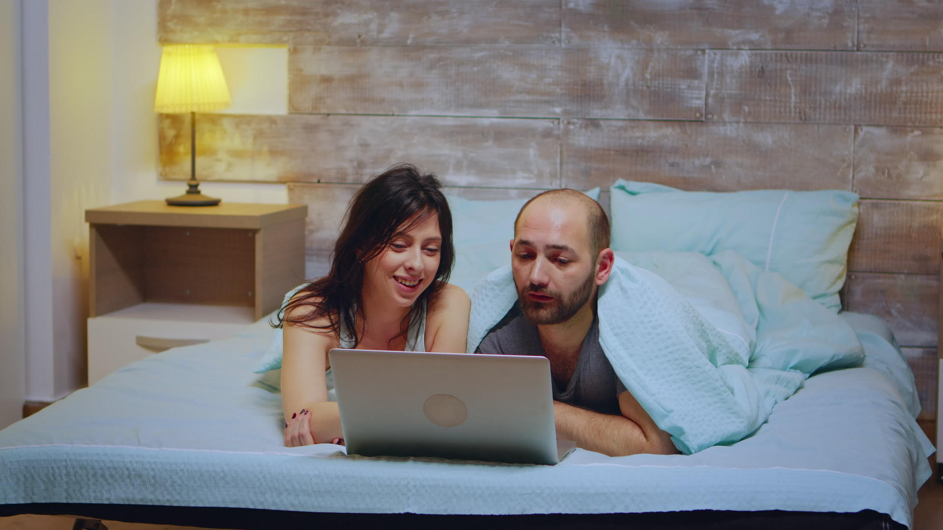 一对夫妇穿着睡衣躺在床上用笔记本电脑购物视频的预览图