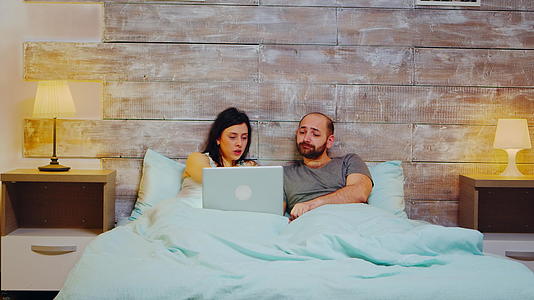 这对穿着睡衣的年轻夫妇深夜在笔记本电脑上购物视频的预览图