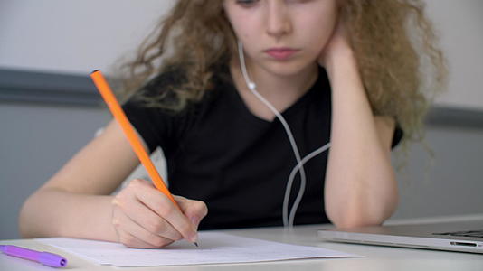 少女在耳机里听音乐用铅笔在纸上写字视频的预览图
