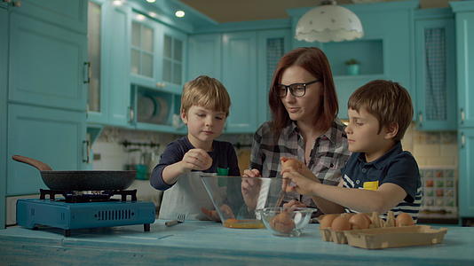 母亲和两个儿子在家里的蓝色厨房里打鸡蛋视频的预览图