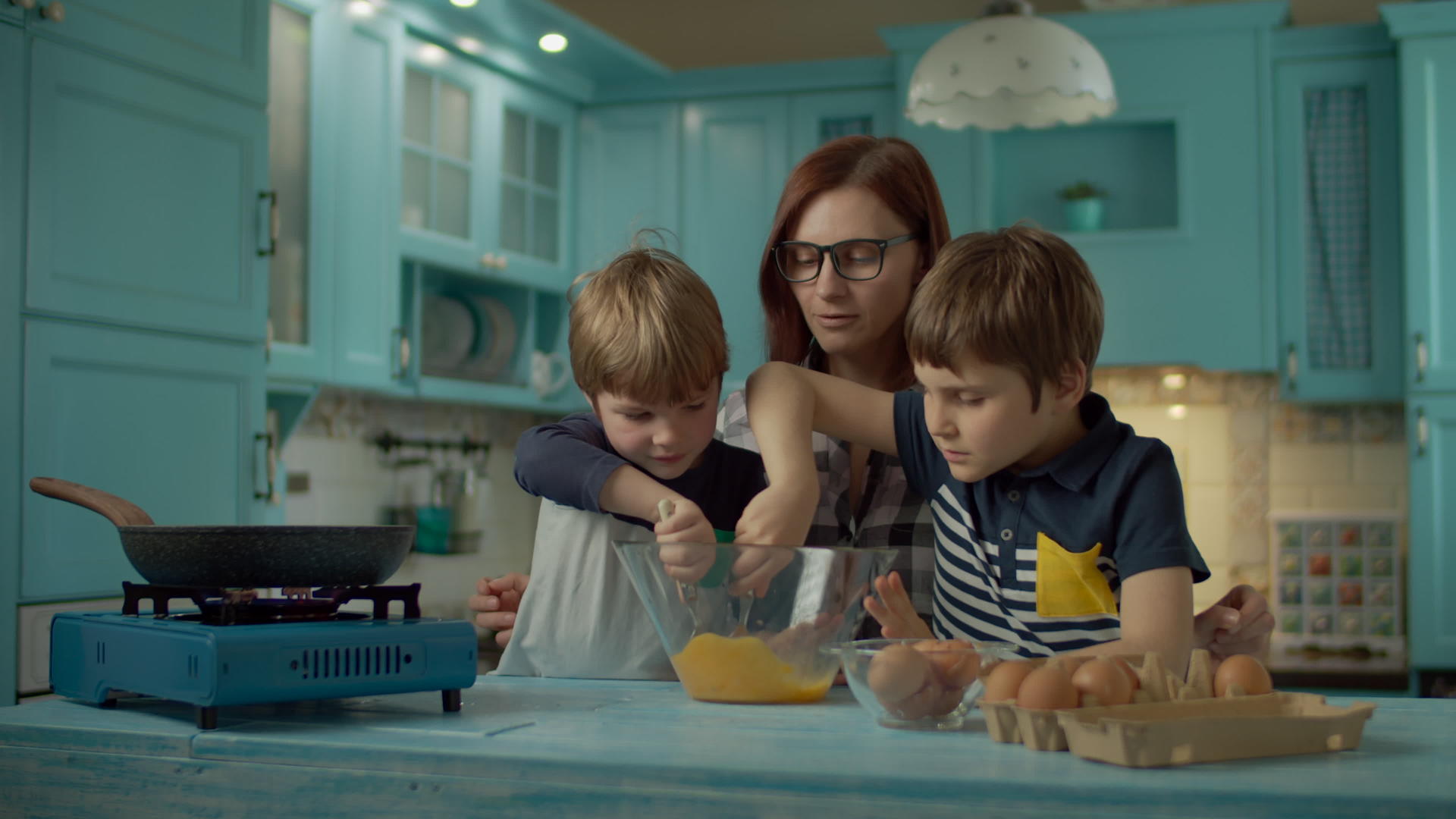 在家里的蓝色厨房里母亲和两个儿子一起煮炸鸡蛋视频的预览图