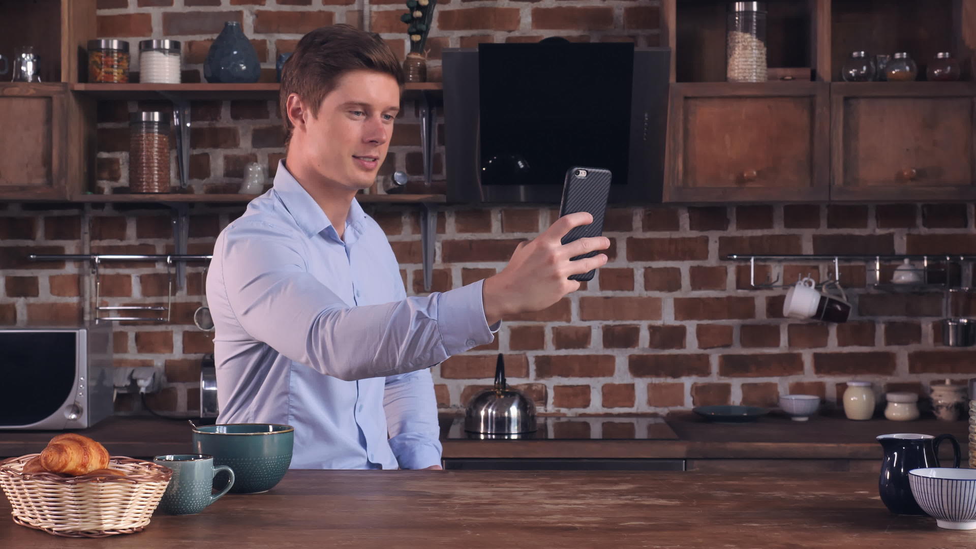 英俊的男人在厨房里用手机视频的预览图
