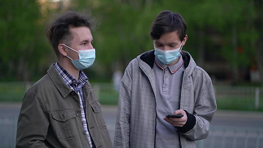 两个戴着医用面具的朋友在户外见面时说话视频的预览图