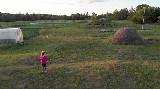 日落时穿着粉色连帽的女孩在干草堆附近跑步和发射滑翔机视频的预览图