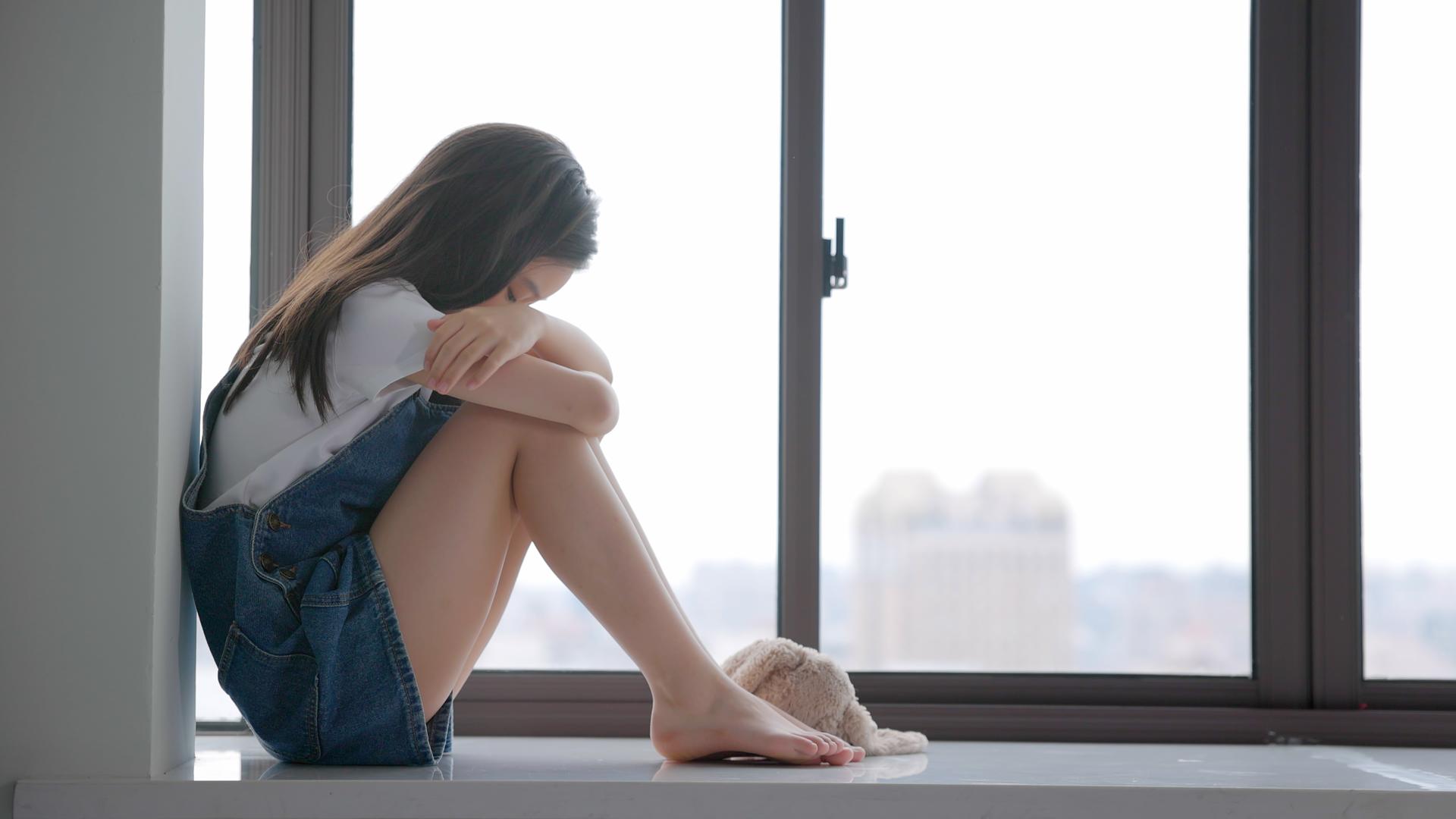 孤独小女孩坐在窗台上将头埋在膝盖上视频的预览图