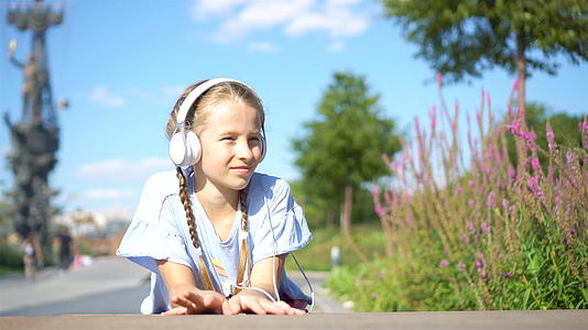 可爱的小女孩在公园里听音乐视频的预览图