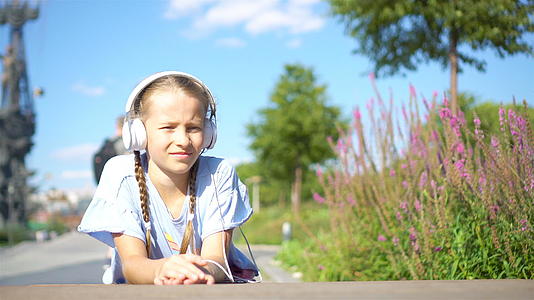 可爱的小可爱女孩在公园外听音乐视频的预览图