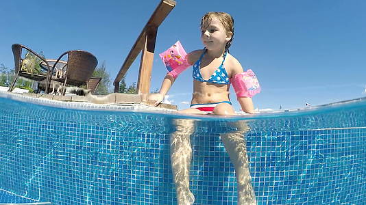 这个可爱的小女孩戴着臂带在游泳池边缘享受着欢笑水下风景很慢视频的预览图
