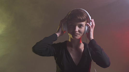 一个可爱的女孩戴着耳机跳舞烟雾侧色彩鲜艳的背景视频的预览图