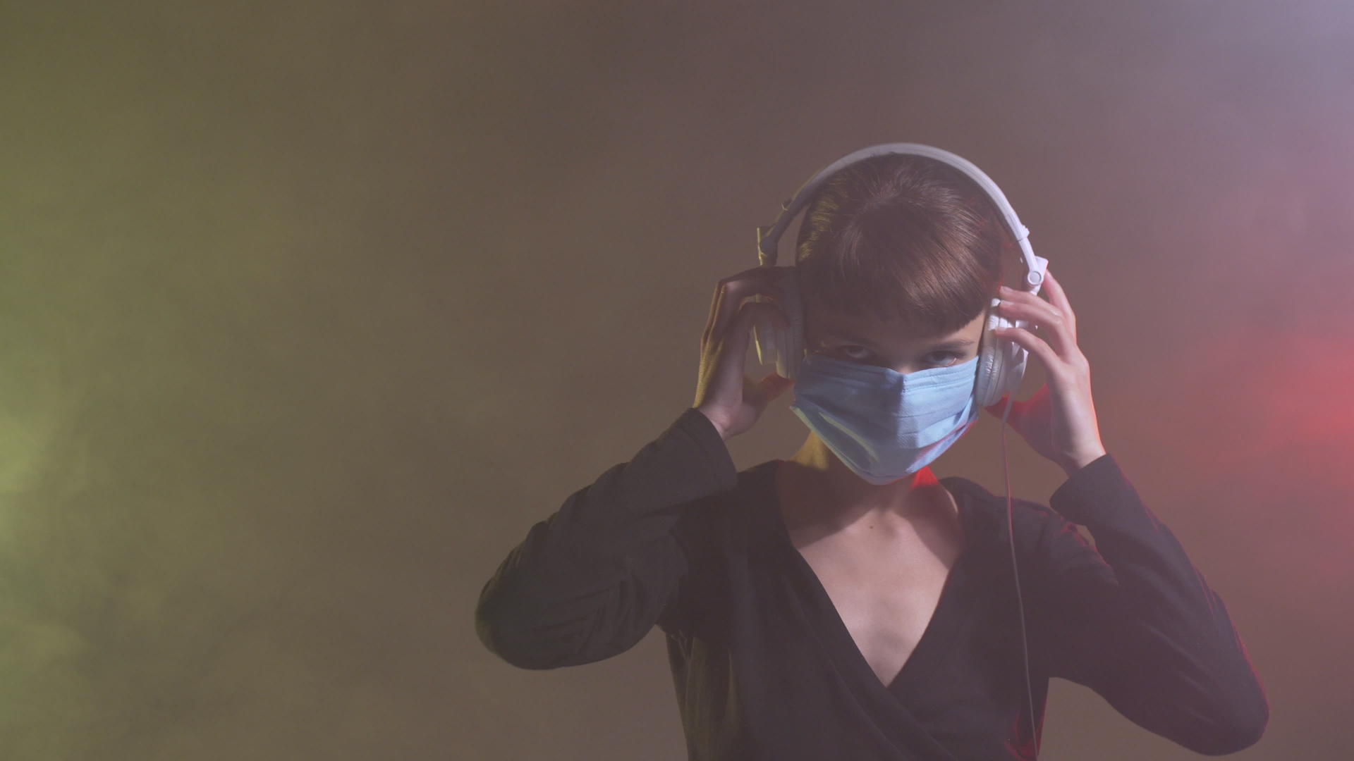 一个可爱的女孩戴着耳机和医疗面具跳舞烟雾彩鲜艳的背景视频的预览图
