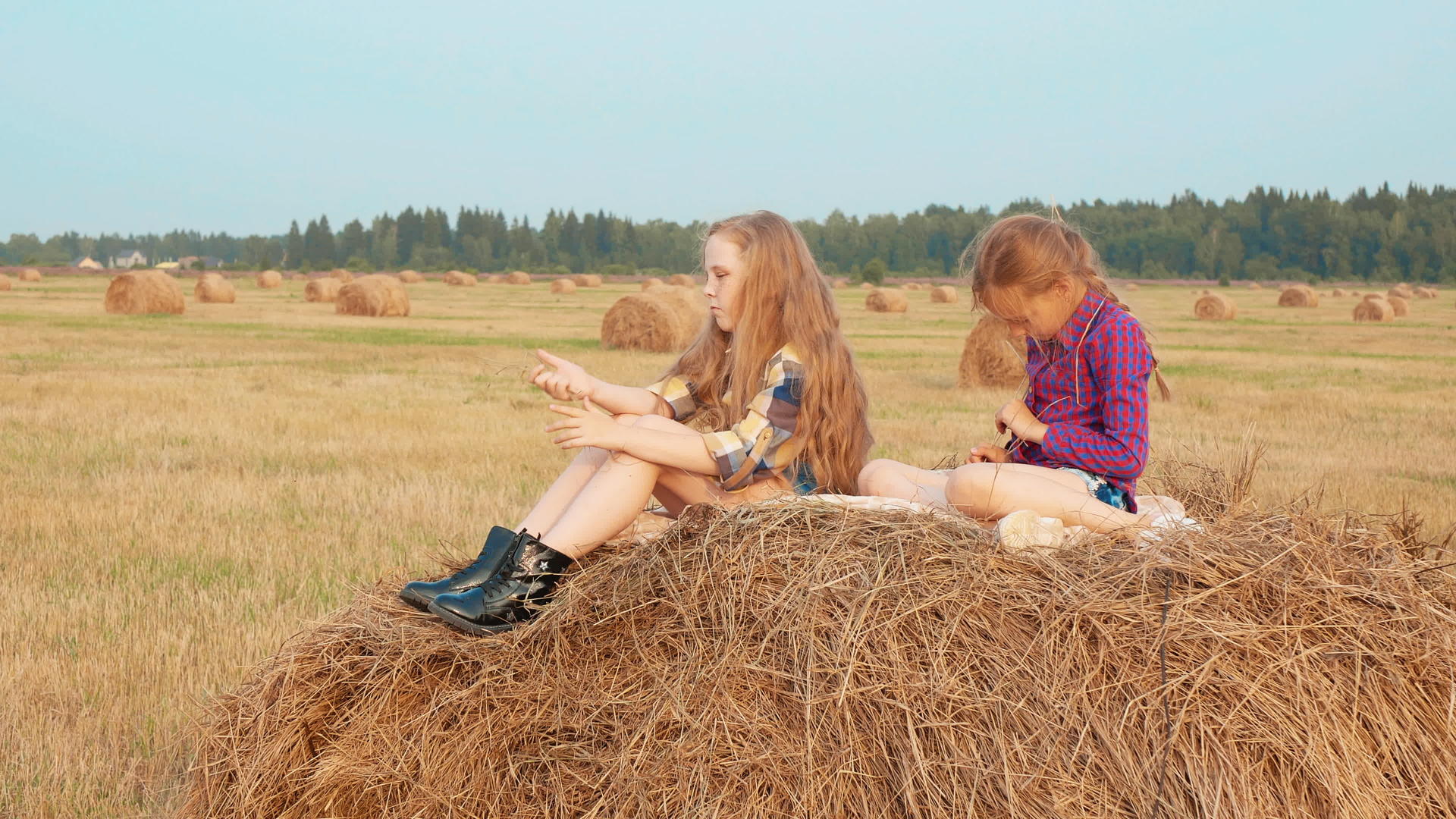 可爱的女孩坐在干草堆上玩野外游戏视频的预览图