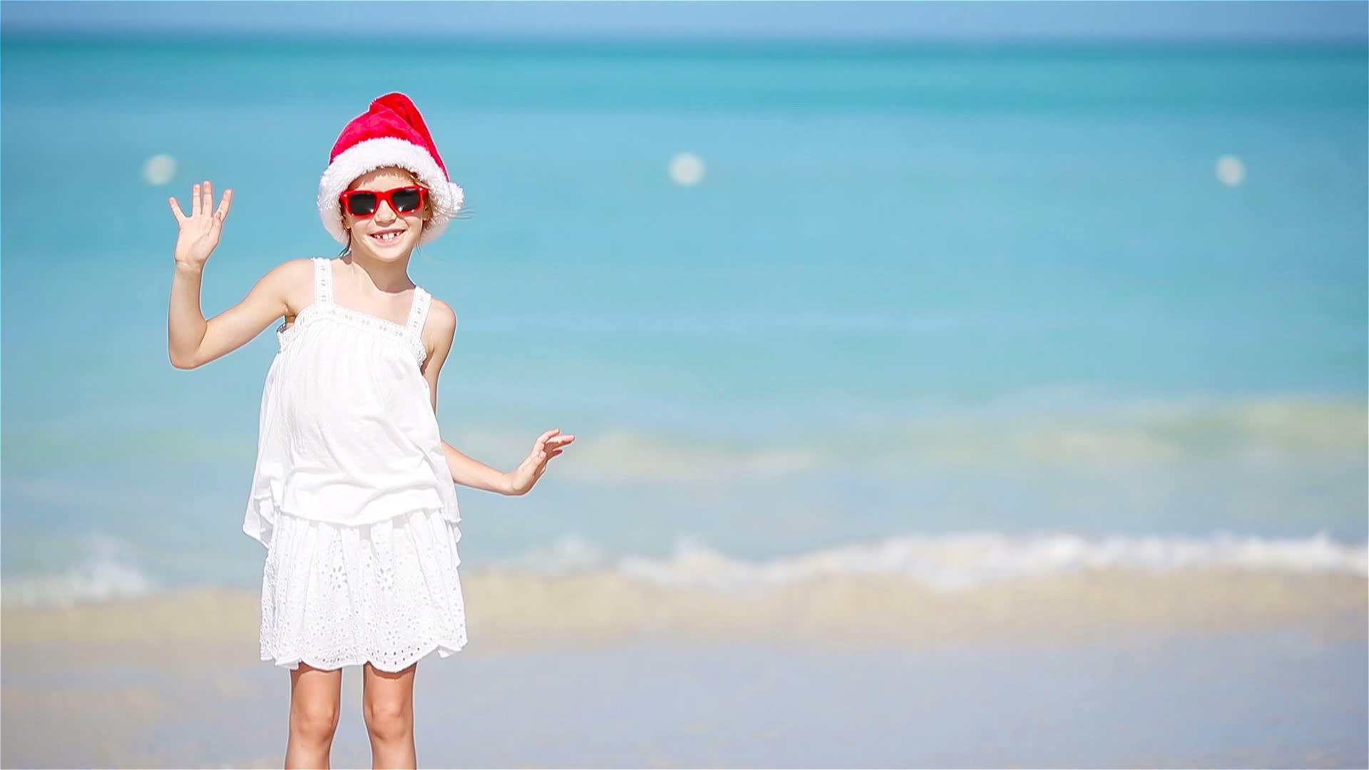 可爱的小女孩戴着圣诞帽子在白色的海滩上视频的预览图