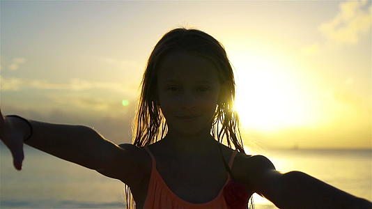 白色沙滩上日落时可爱快乐的小女孩视频的预览图