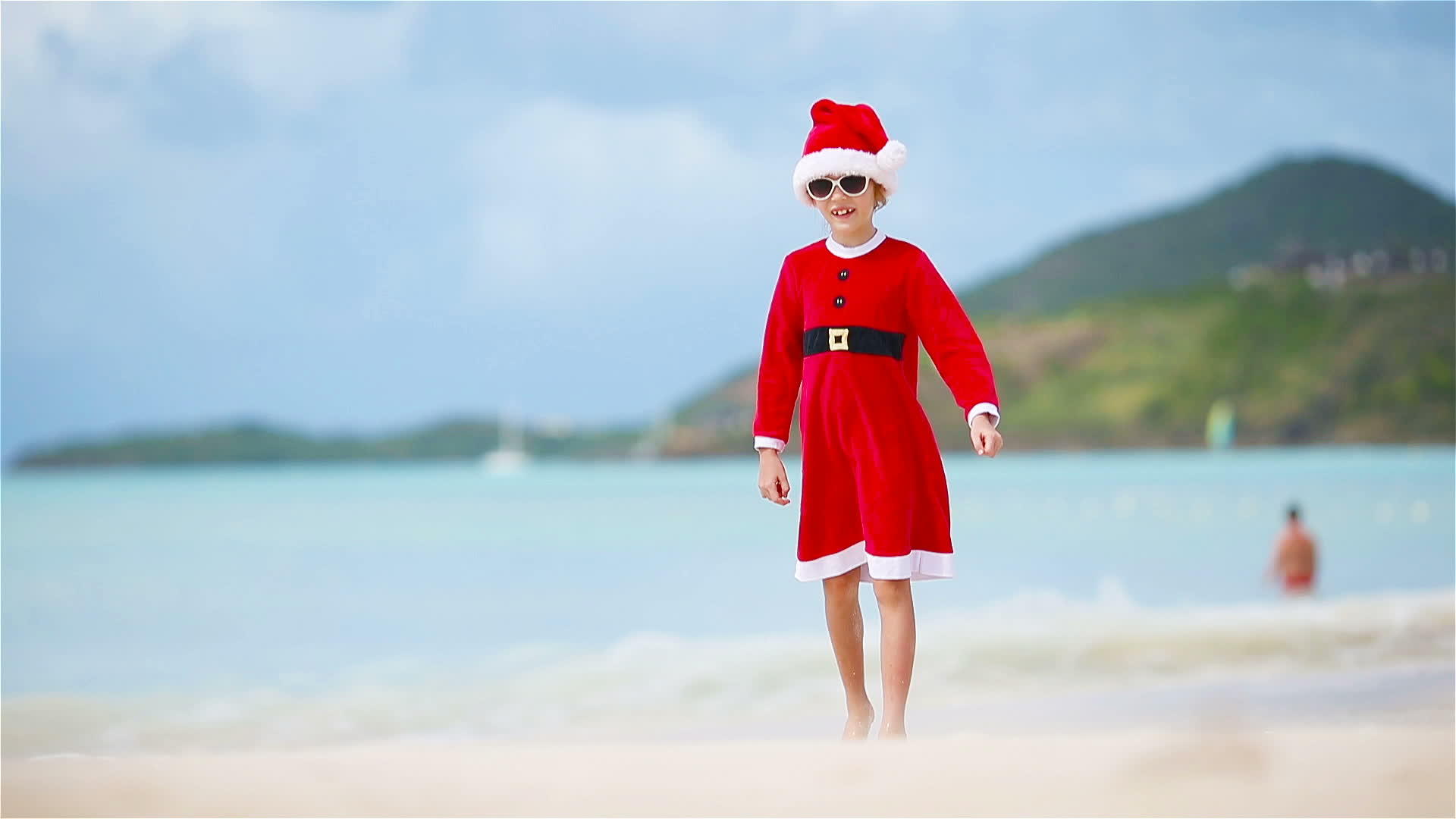 圣诞节期间可爱的女孩在白色海滩上戴着圣诞帽子视频的预览图