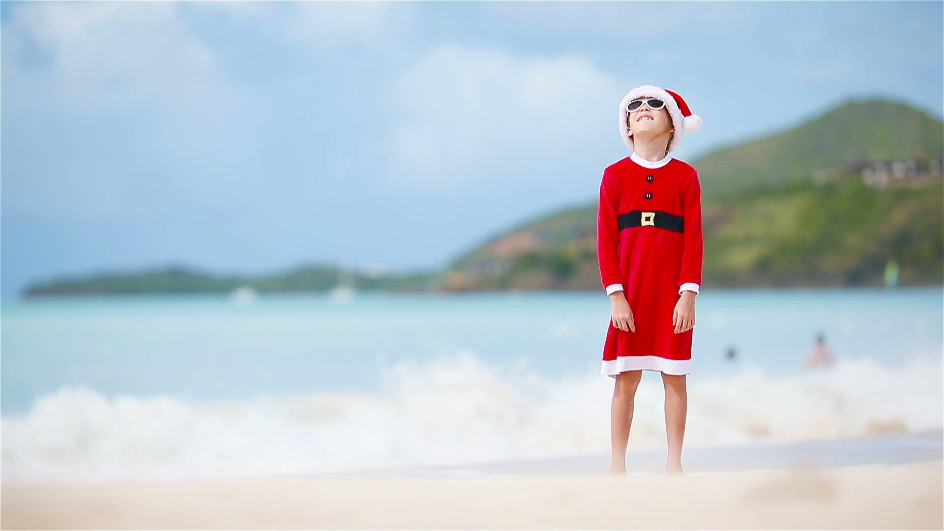 圣诞节期间可爱的小女孩在白色海滩上戴着圣诞帽子视频的预览图