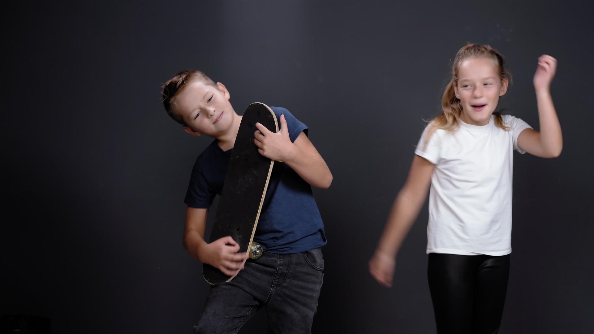 小男孩假装用滑板弹吉他姐姐或朋友女孩在他旁边跳舞视频的预览图