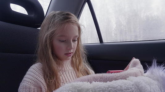 长发可爱的小女孩开车旅行使用智能手机视频的预览图
