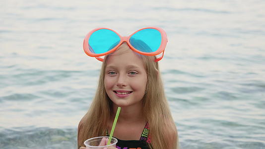可爱快乐的女孩在海边的塑料杯里喝鸡尾酒视频的预览图
