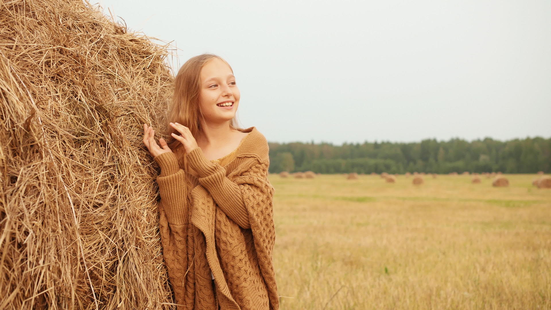 可爱的快乐女孩站在田野里的干草堆附近视频的预览图