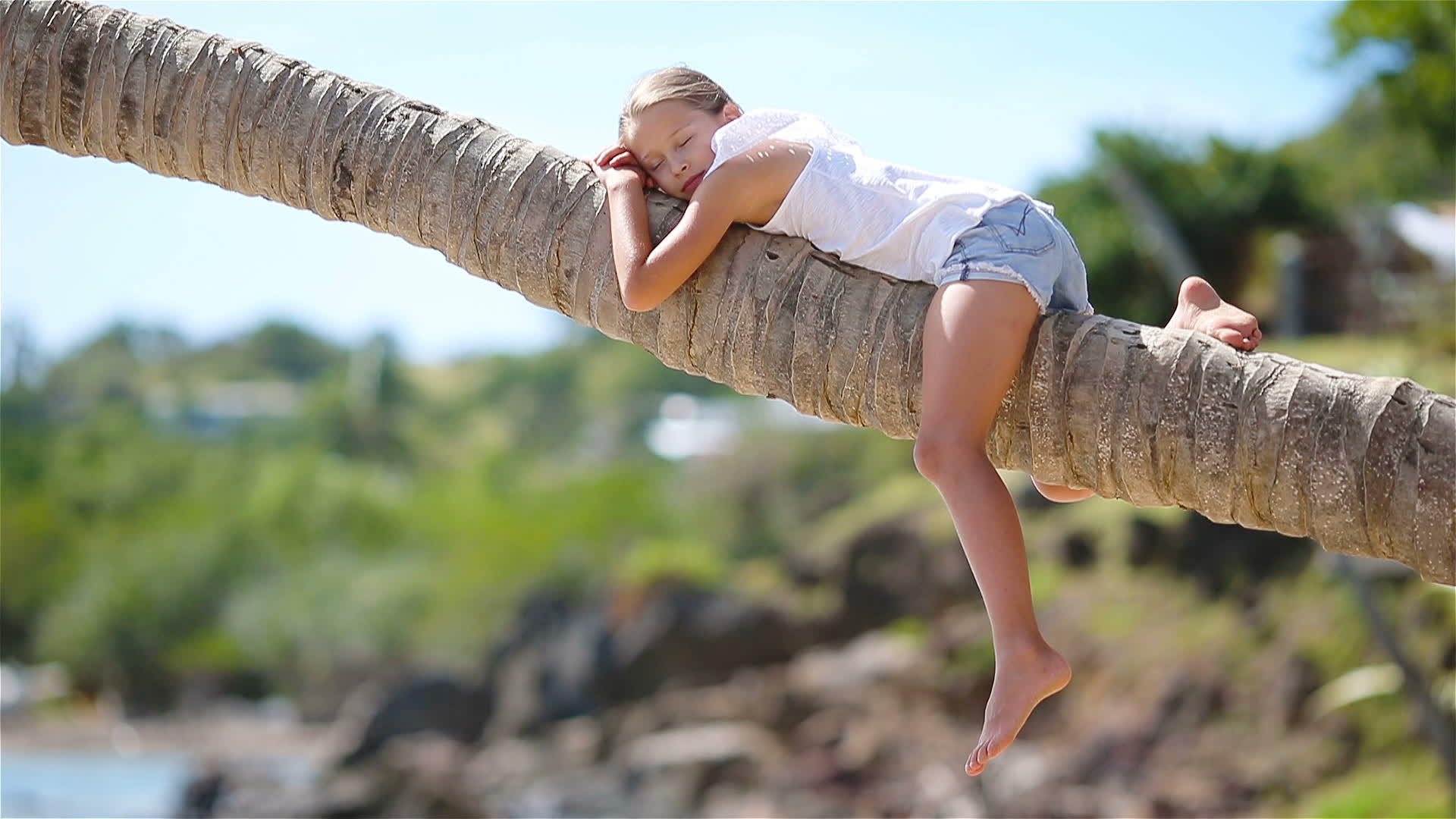 暑假期间热带海滩上可爱的小女孩坐在棕榈树上视频的预览图