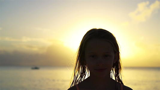 小女孩的肖像看着镜头和微笑的背景美丽的天空和海洋的笑声视频的预览图