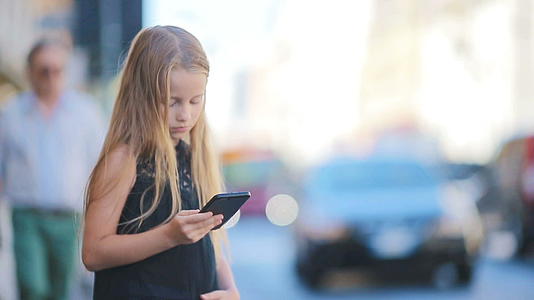 可爱的小女孩在温暖的欧洲城市的户外日间使用手机视频的预览图