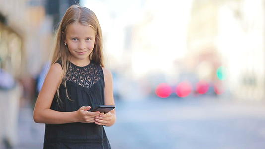可爱的小女孩聪明的手机在温暖的欧洲城市户外温暖的日子视频的预览图