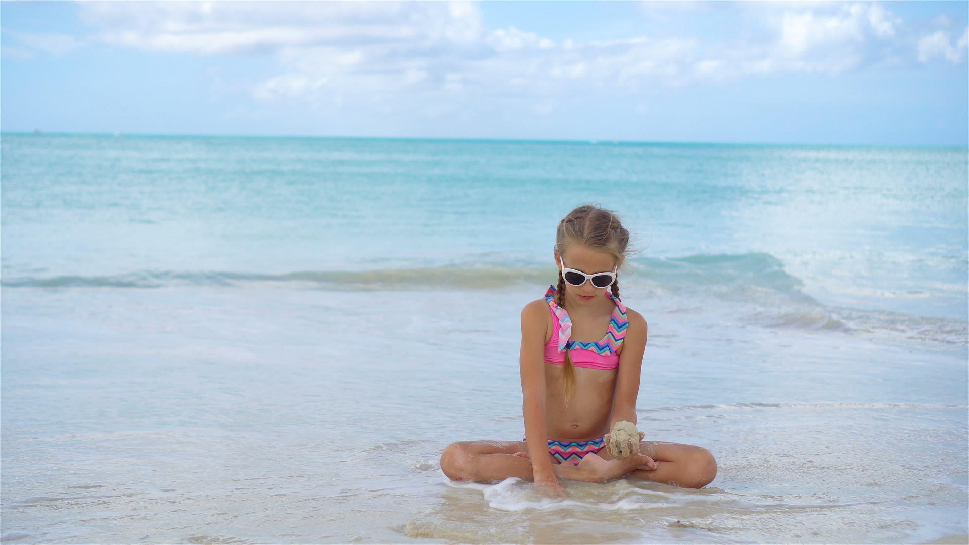 可爱活跃的小女孩坐在沙滩上视频的预览图