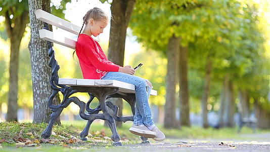 秋天带着智能手机的可爱小女孩在阳光温暖的秋天出门视频的预览图