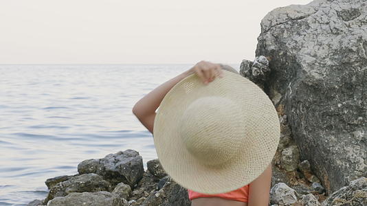在比基尼一个可爱的女孩试图在海里的石头上画一幅美丽的草帽肖像视频的预览图