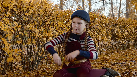 可爱的女孩红发辫子在秋天的公园里扔黄叶快乐的女孩视频的预览图
