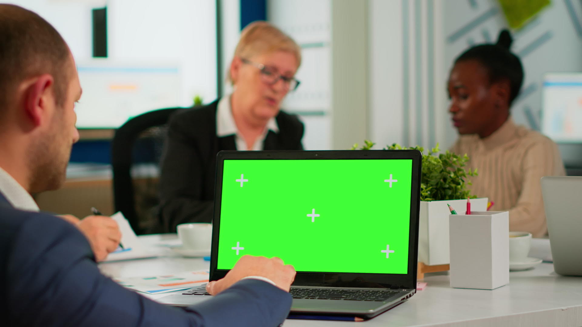 坐在会议桌上的商务人员使用带有绿色屏幕的笔记本电脑视频的预览图