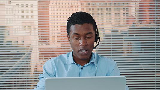 黑人黑人在耳机上和某人说话在电脑上工作视频的预览图
