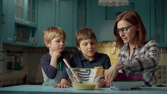 一位30多岁的年轻母亲带着两个孩子在家里的蓝色厨房里使用华夫的蓝色厨房视频的预览图