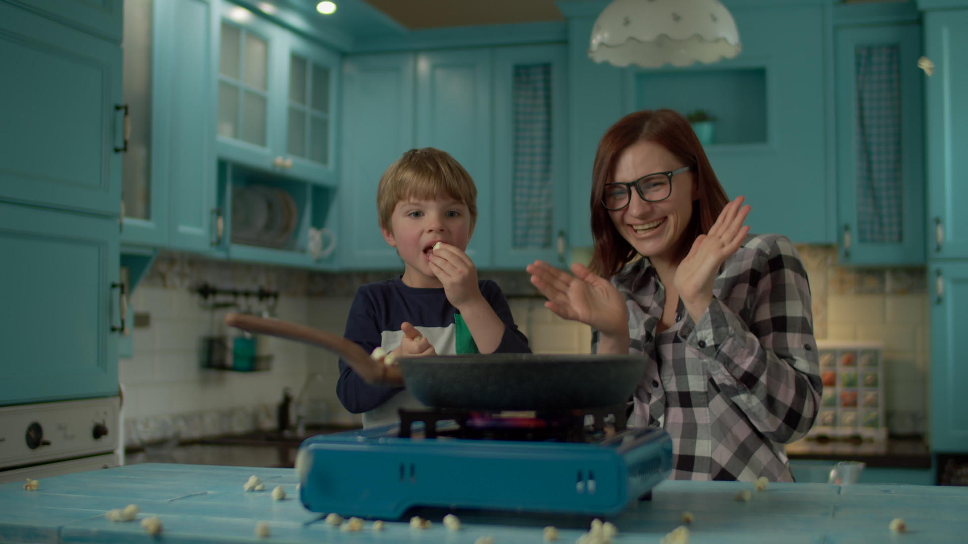 年轻的母亲和儿子在蓝色厨房的煎锅里煮爆米花视频的预览图