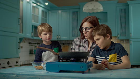 年轻的母亲和两个儿子在家煮爆米花视频的预览图