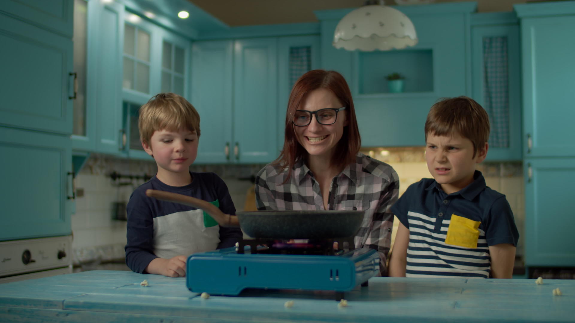 年轻的母亲和两个儿子的幸福家庭在家里的蓝色厨房里做爆米花视频的预览图