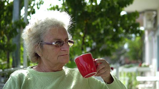 老年妇女坐在户外喝咖啡茶视频的预览图