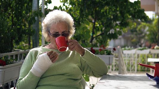 受伤的老年妇女坐在户外喝咖啡视频的预览图