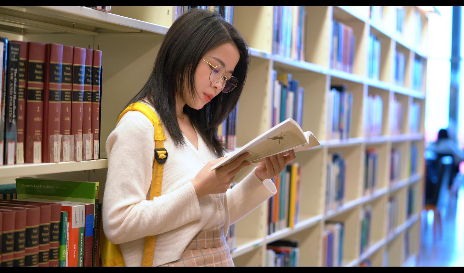 4k背书包的女生靠在书架上看书视频的预览图