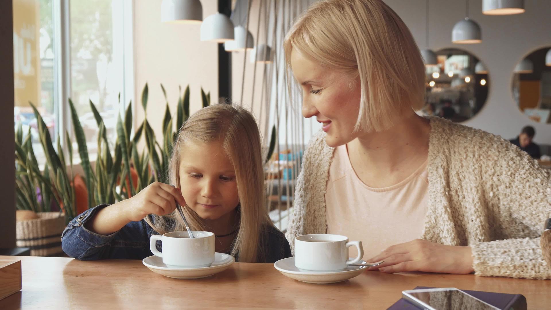 女人把勺子放在咖啡馆的女儿杯里视频的预览图
