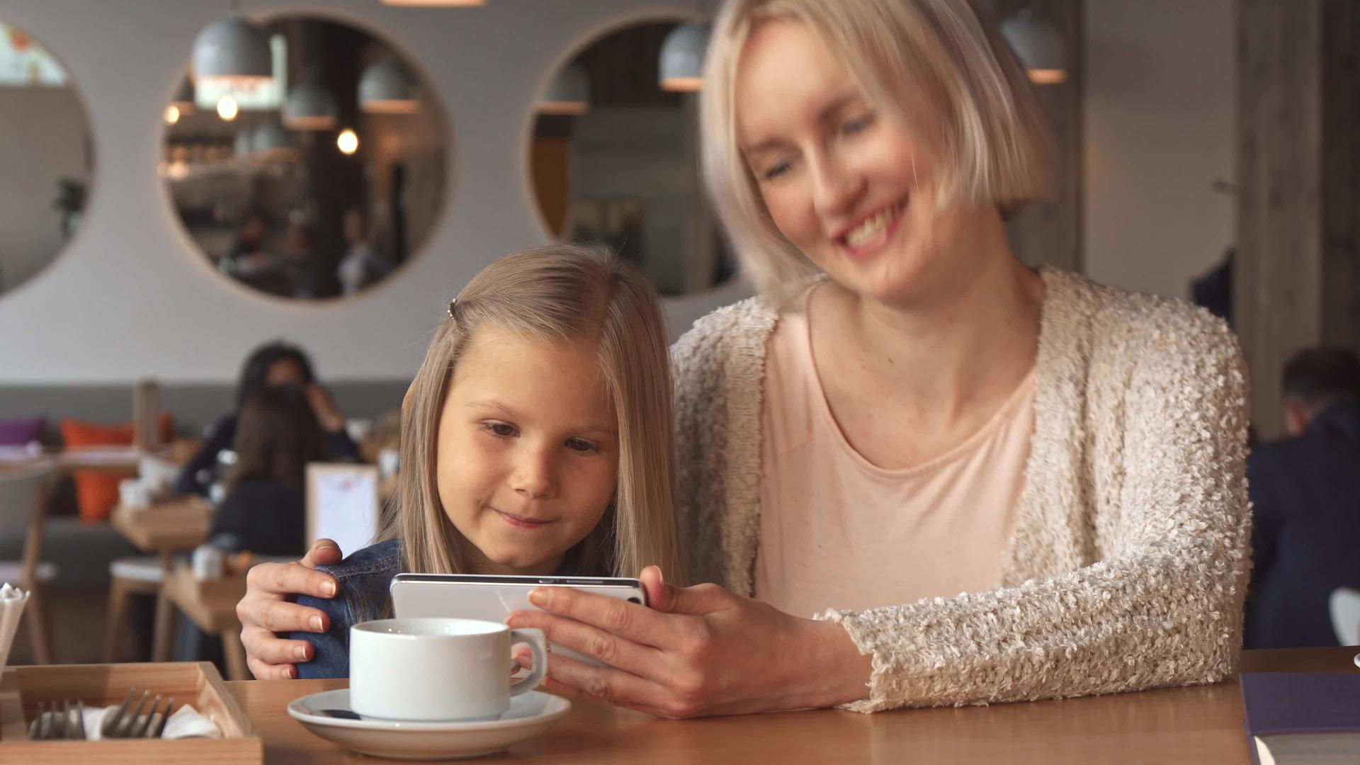 母亲和女儿在咖啡馆使用智能手机视频的预览图
