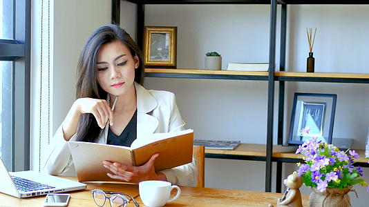 美丽的亚洲女商人早上坐在笔记本电脑前在工作区看书视频的预览图