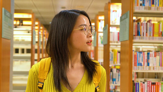 4k戴眼镜的女学生在图书馆里行走找书视频的预览图