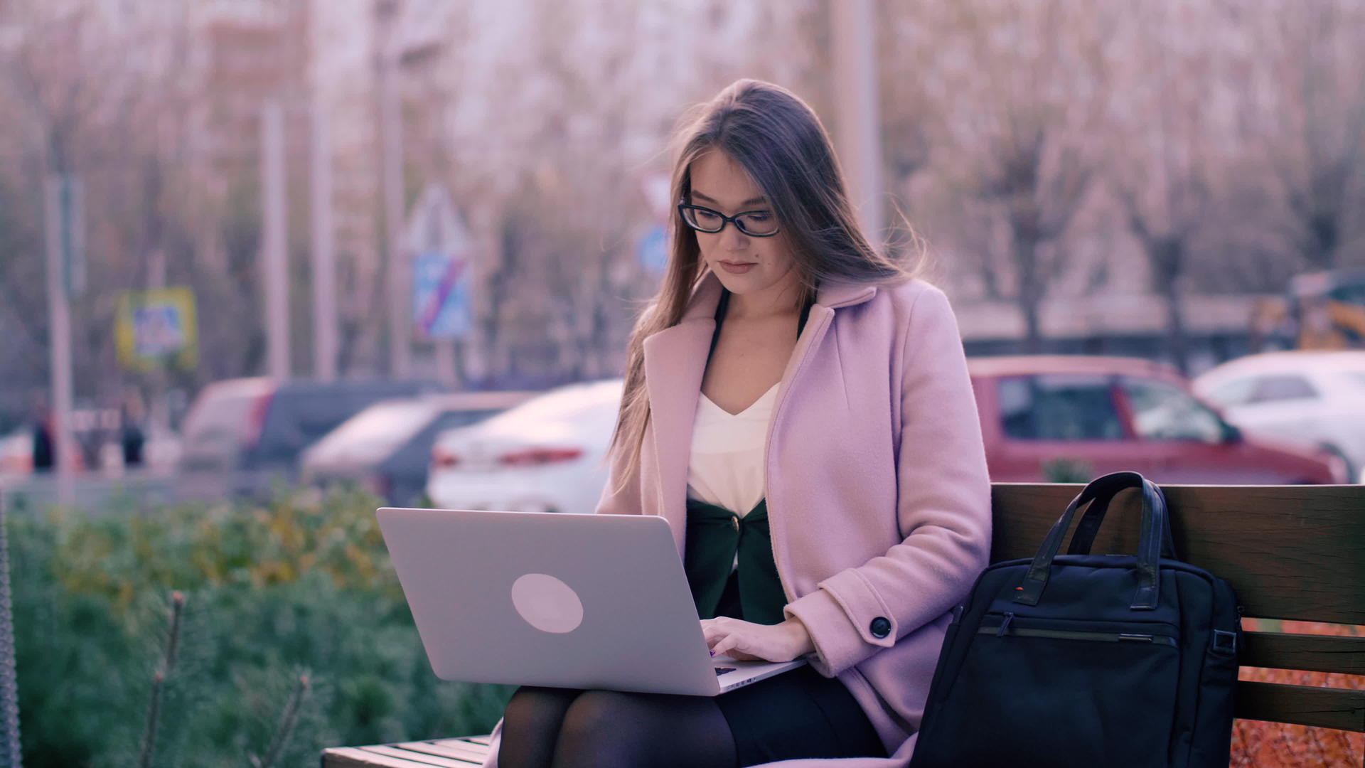 女性坐在长椅上在城市公园的背景下使用笔记本电脑视频的预览图