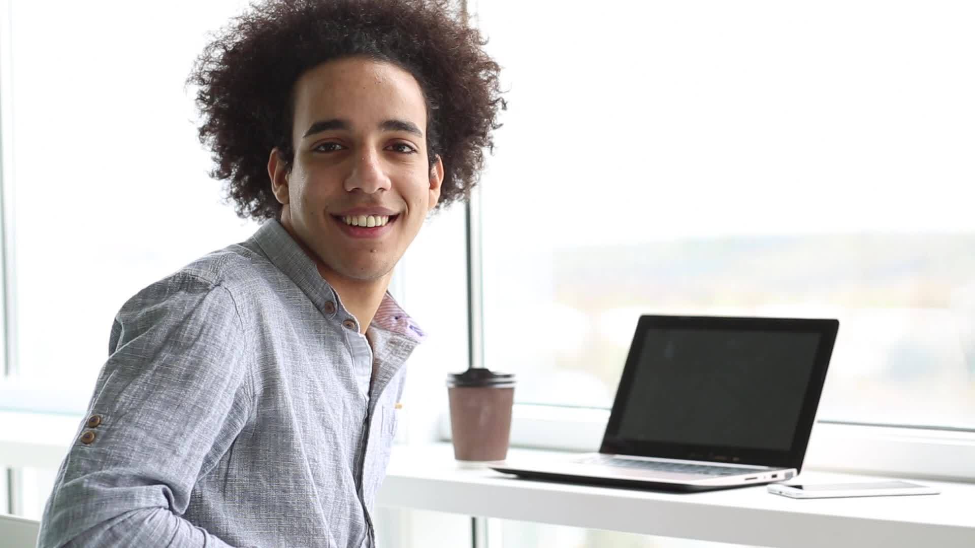 一个微笑的年轻人在笔记本电脑上工作视频的预览图